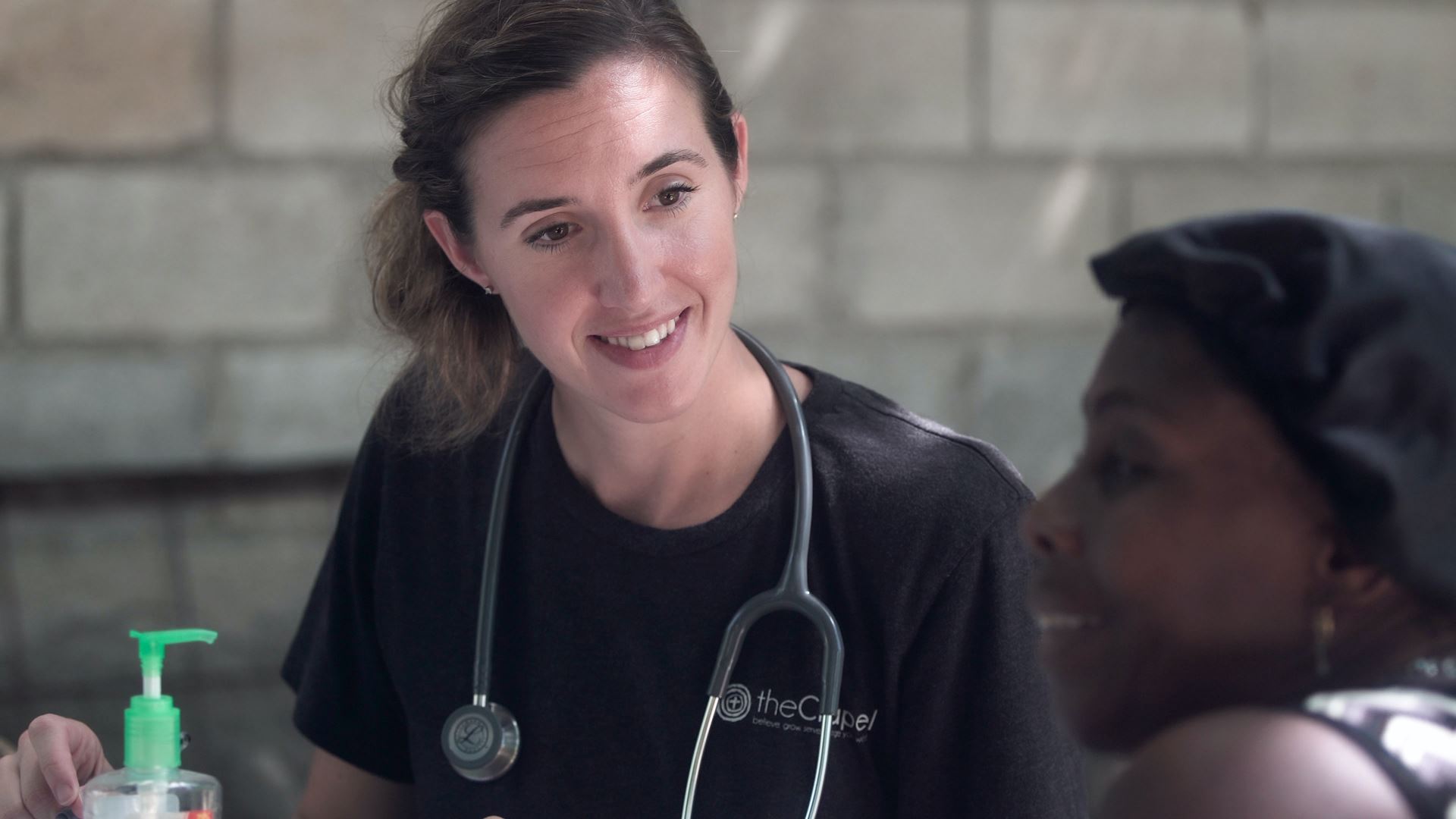 A woman with a stethoscope around her neck, smiling at a patient sitting down